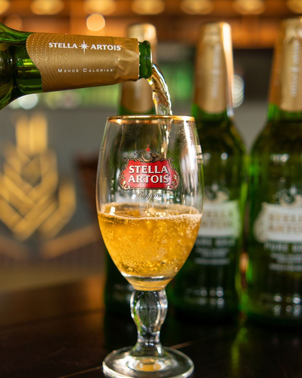 Cerveja sendo servida na taça diante das garrafas geladas do balcão