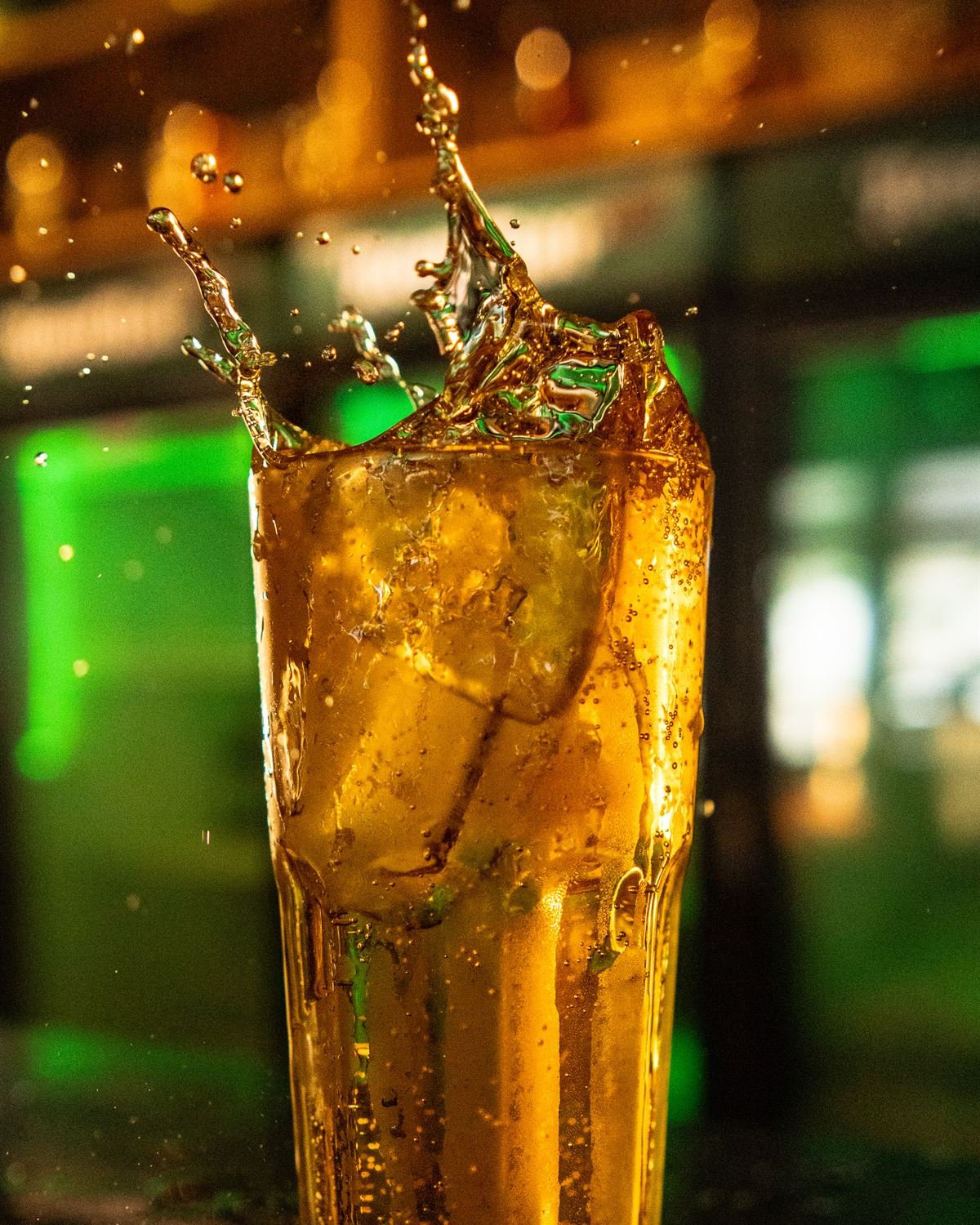 Copo alto de drink com gelo respingando sobre o balcão do bar