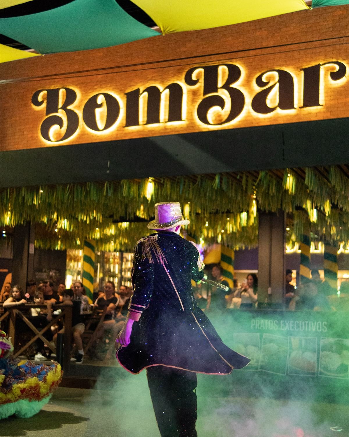 Fachada iluminada do BomBar em noite de festa, com fumaça colorida na calçada